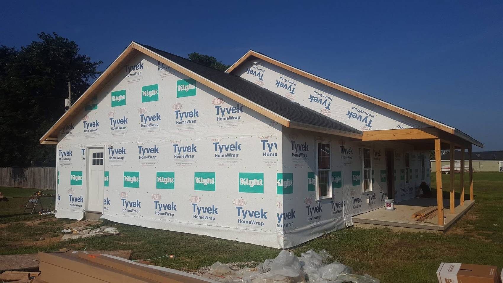 Custom home exterior wrapped in house wrap with shingled roof and covered porch nearing completion