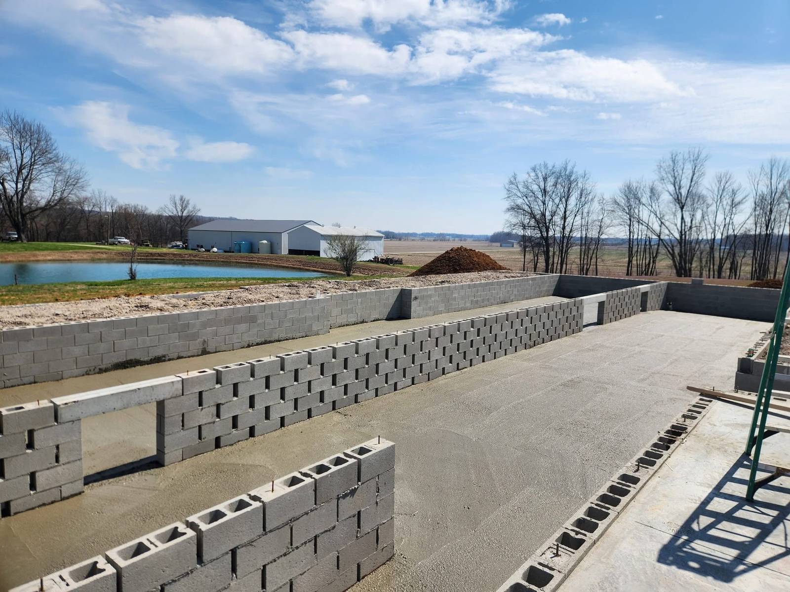 Custom home foundation walls under construction on a rural property with a pond