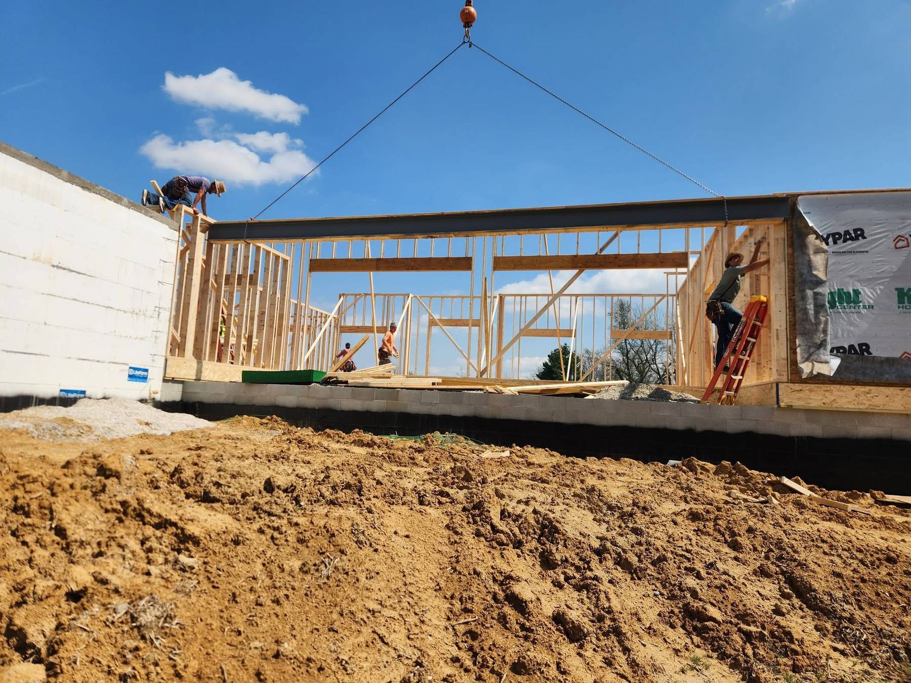 Crane setting a structural beam while a crew frames a custom home built by Hurt & Sons Construction